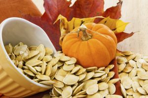 Colorful autumn still life with a yellow bowl overflowing with pumpkin seeds