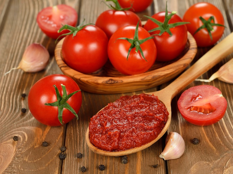 tomato paste in wooden spoon on brown background